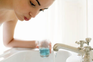 Young woman rinsing mouth, leaning over sink, close-up